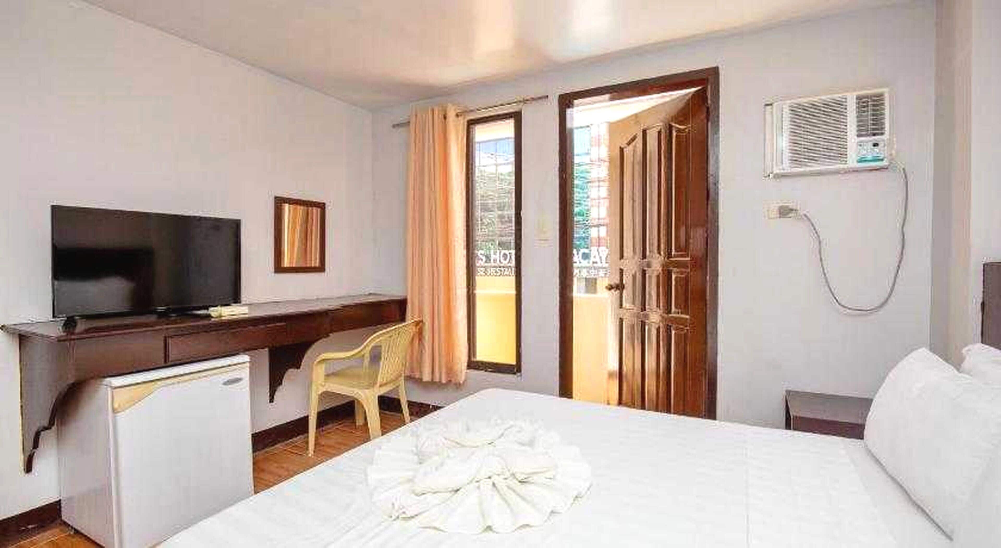 Une chambre d’hôtel avec un lit, un bureau avec une télévision, une chaise et une porte-fenêtre donnant sur un balcon.