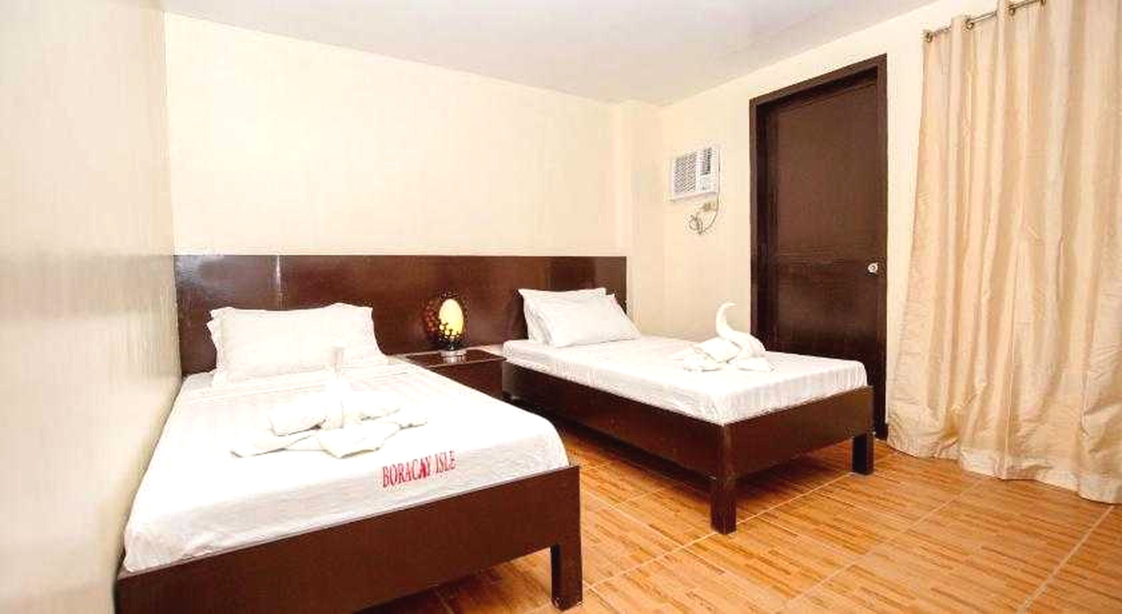 Habitación de hotel con dos camas, suelo de madera, una puerta y una cortina.