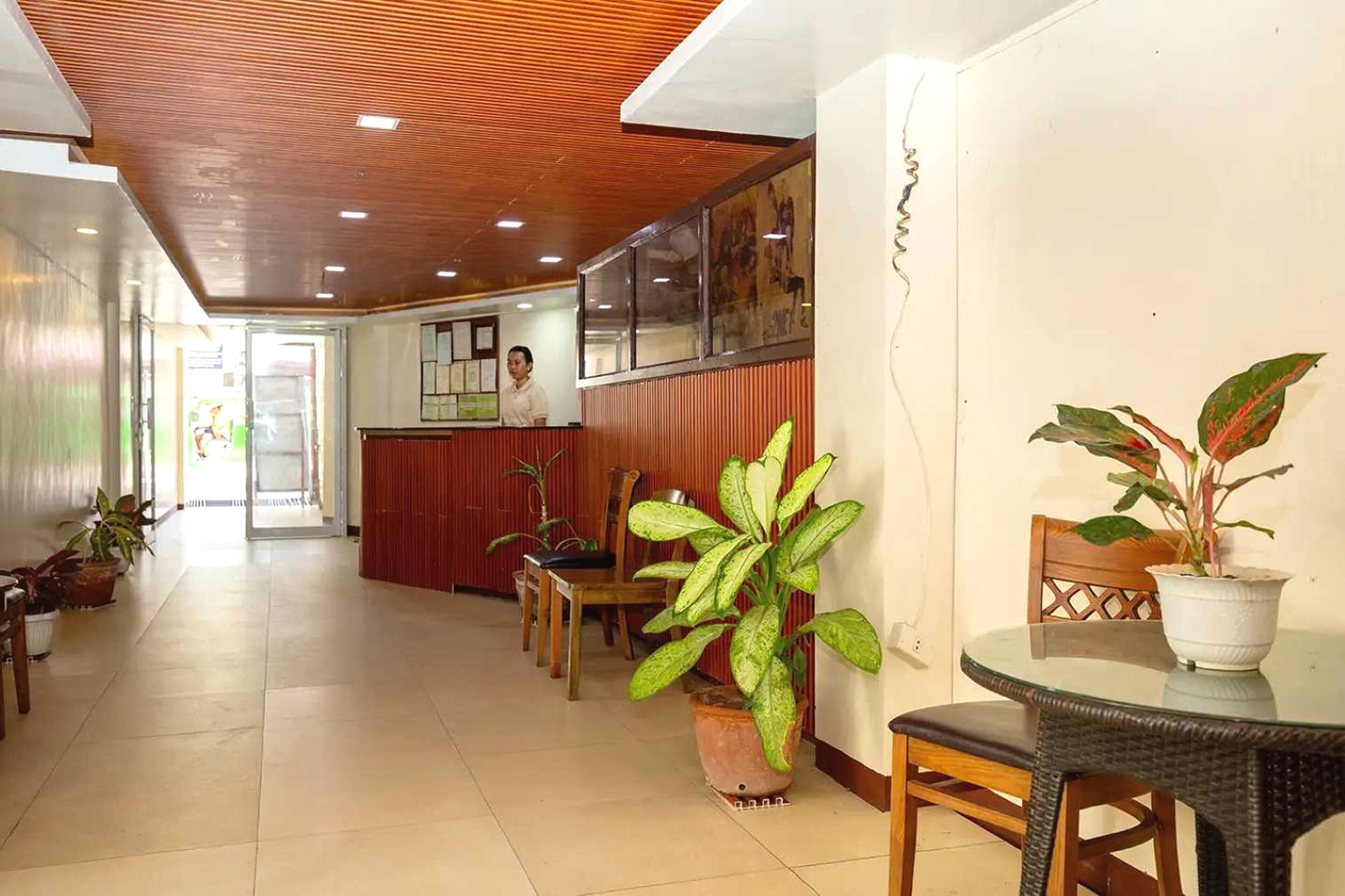 A hotel lobby with a wooden ceiling, a reception desk, several chairs, and potted plants.