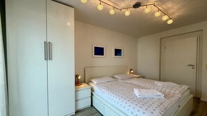 A bedroom with a bed, bedside tables, a wardrobe, and a ceiling light fixture. - Apartment 'Traveperle 1' with Private Terrace and Wi-Fi (Lübeck)