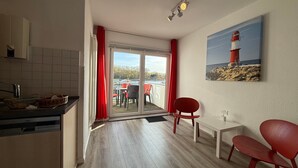 A modern kitchen with a dishwasher, a dining area with a table and chairs, a sliding glass door leading to an outdoor deck, and a painting of a lighthouse on the wall. - Apartment 'Traveperle 1' with Private Terrace and Wi-Fi (Lübeck)