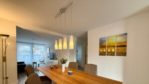 A modern dining area with a wooden table, chairs, hanging pendant lights, a vase with flowers, and a painting on the wall. - Apartment 'Traveperle 1' with Private Terrace and Wi-Fi (Lübeck)