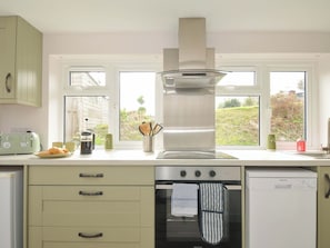A kitchen with a stove, oven, and a window with a view of greenery. - Casa Mia (St Austell)