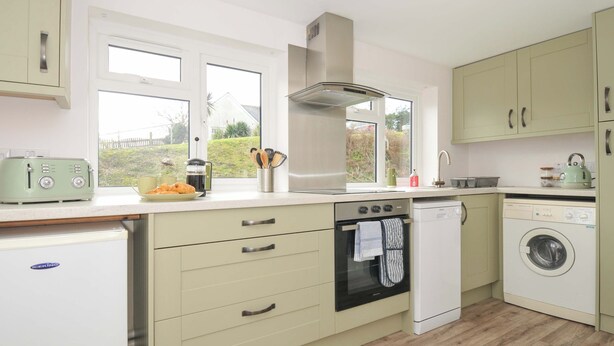 A modern kitchen with a built-in oven, dishwasher, and a window with a view of the outdoors. - Casa Mia (St Austell)