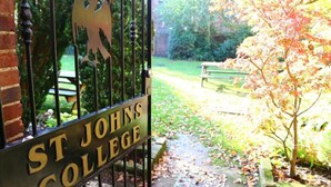 A gate with 'ST JOHNS COLLEGE' sign, a pathway, and a bench in a garden. - St John's College (Durham)