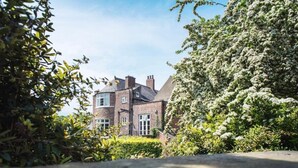 A brick house with a garden and a large tree in the foreground. - St John's College (Durham)