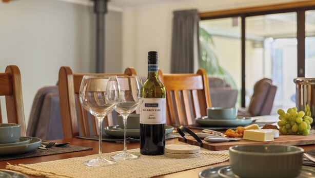 A dining table set with wine glasses, a bottle of wine, cheese, and grapes. - Air on Aldersey (McLaren Vale)