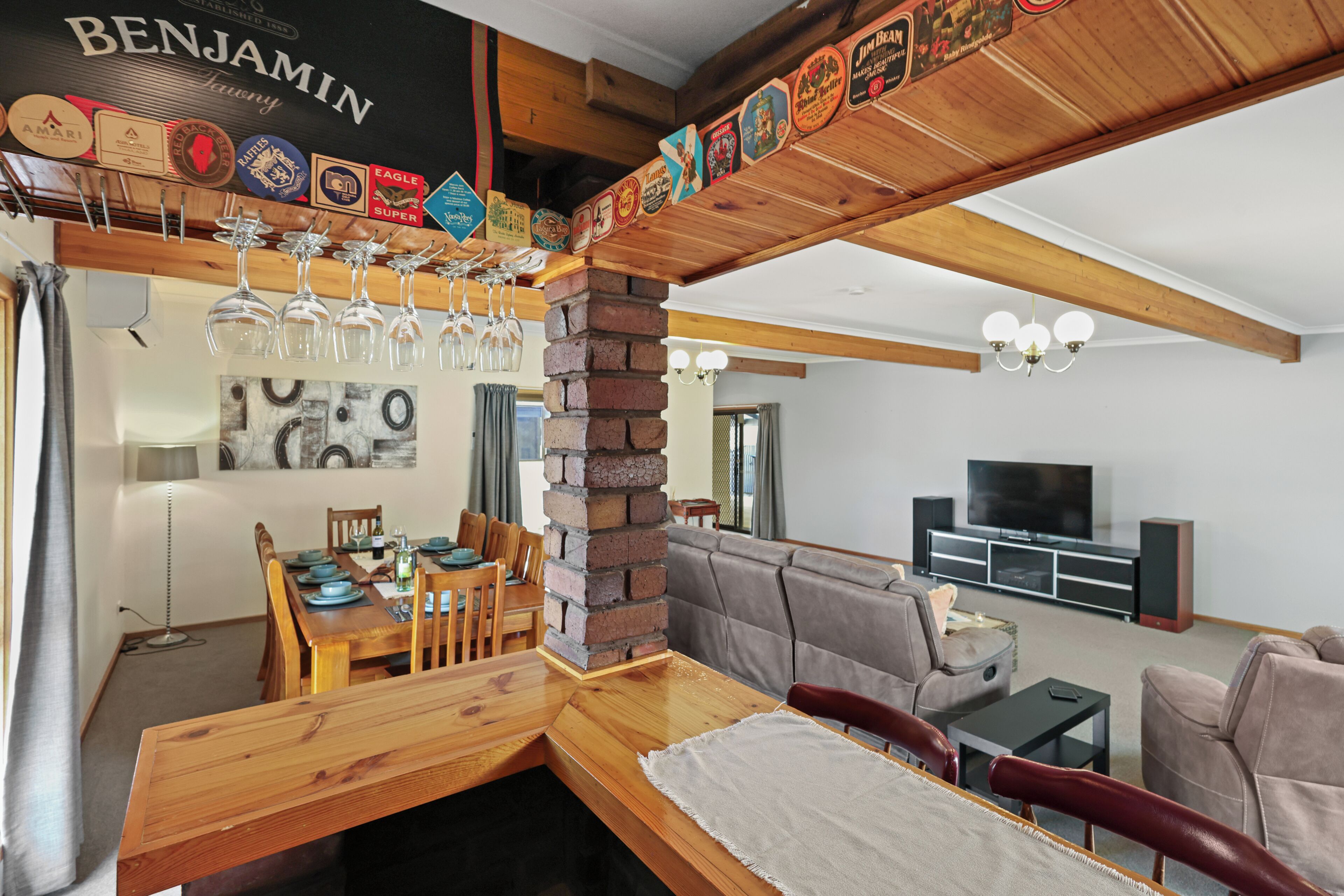 A dining area with a wooden table and chairs, a brick pillar, and a wall-mounted wine glass rack.