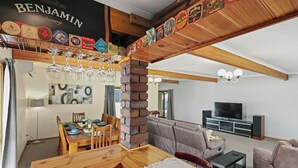 A dining area with a wooden table and chairs, a brick pillar, and a wall-mounted wine glass rack. - Air on Aldersey (McLaren Vale)