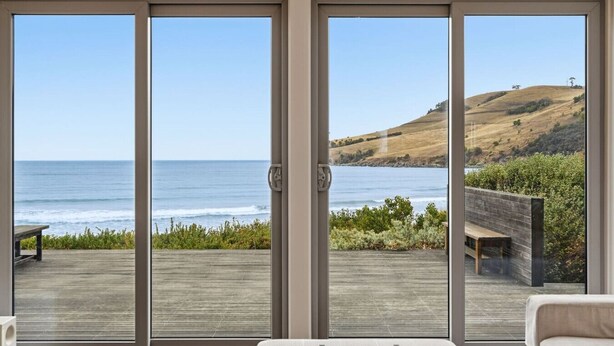 A room with a large sliding glass door leading to a deck with a view of the ocean and hills. - Beachfront Escape in Clifton (Clifton Beach)