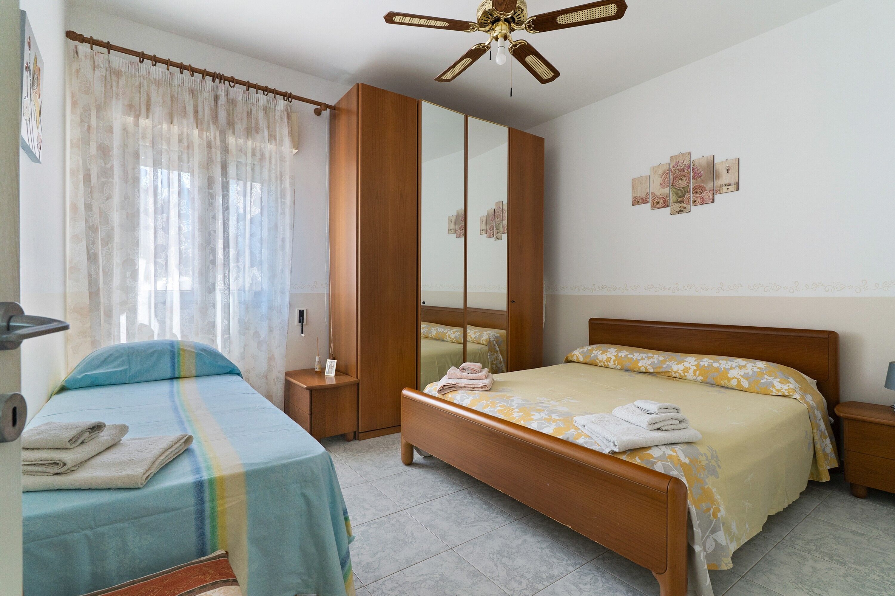 Una camera da letto con un letto, un comodino, un armadio, una ventola a soffitto e una finestra con tende.