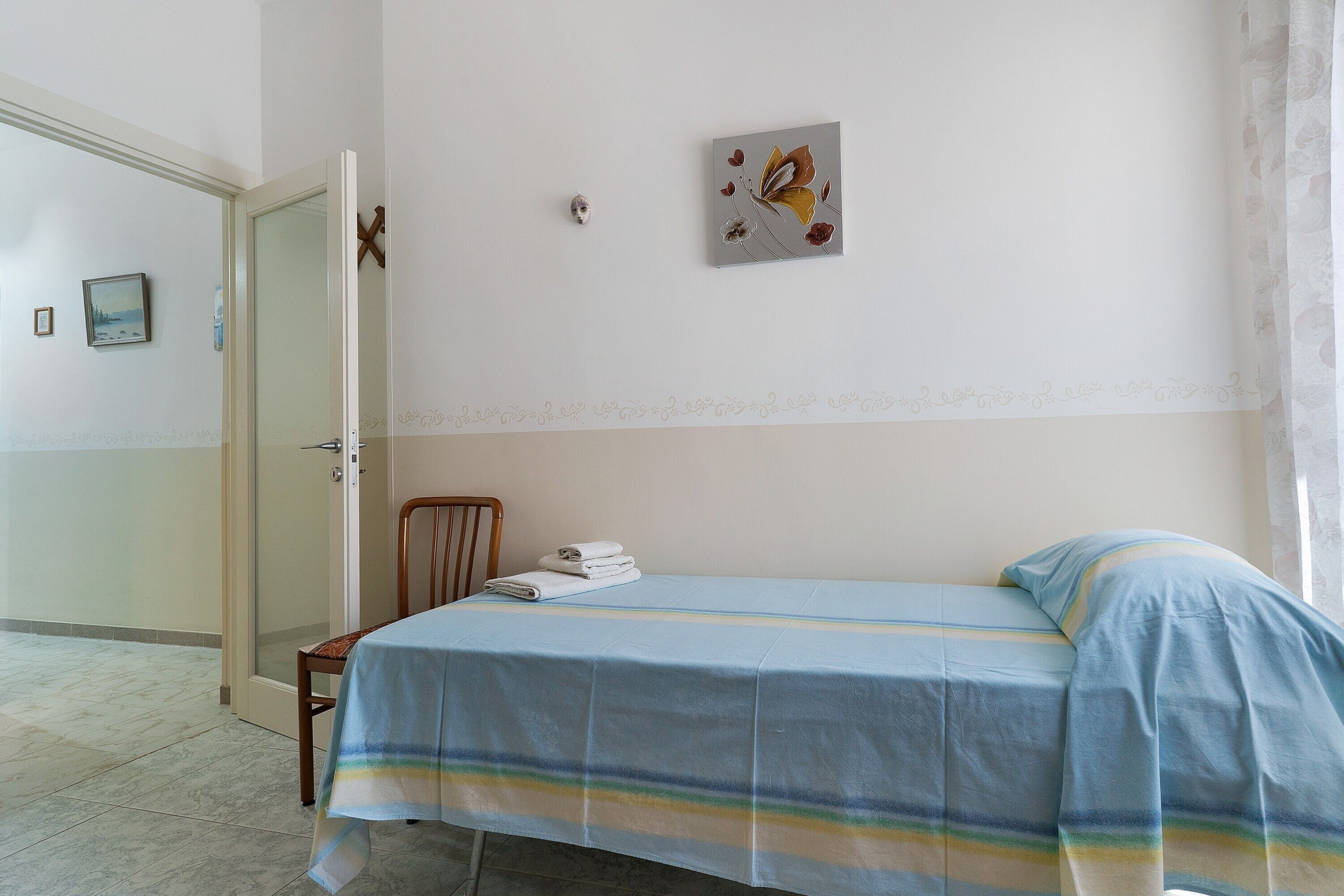 Una stanza con un letto, una sedia, una porta e una parete decorata con un quadro.