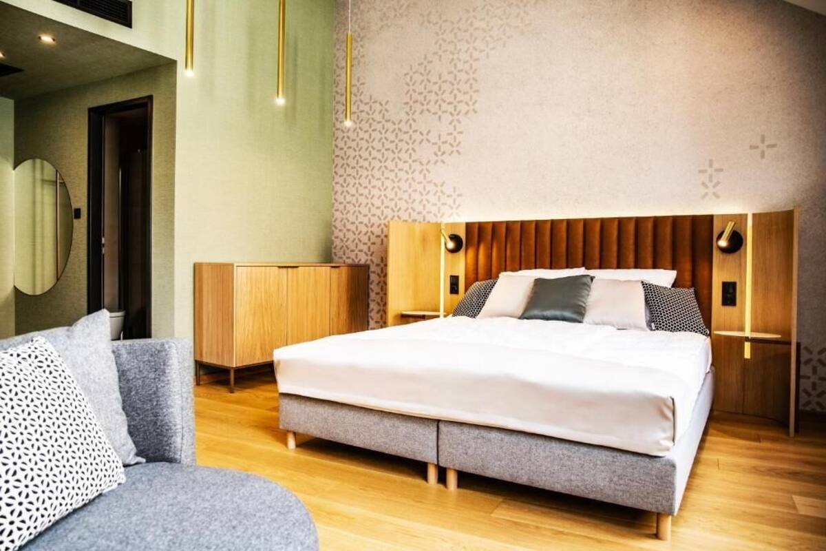 Un dormitorio moderno con cama, sofá, mesita de noche de madera y pared con diseño de hojas.