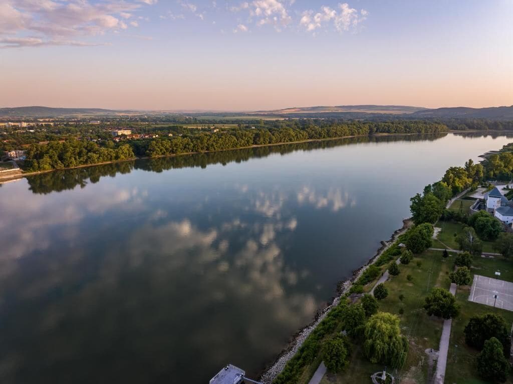 A river with a reflection, surrounded by greenery and buildings.