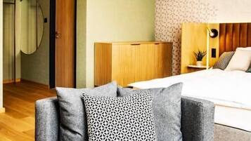 A modern bedroom with a wooden headboard, a grey sofa with patterned cushions, and pendant lighting.