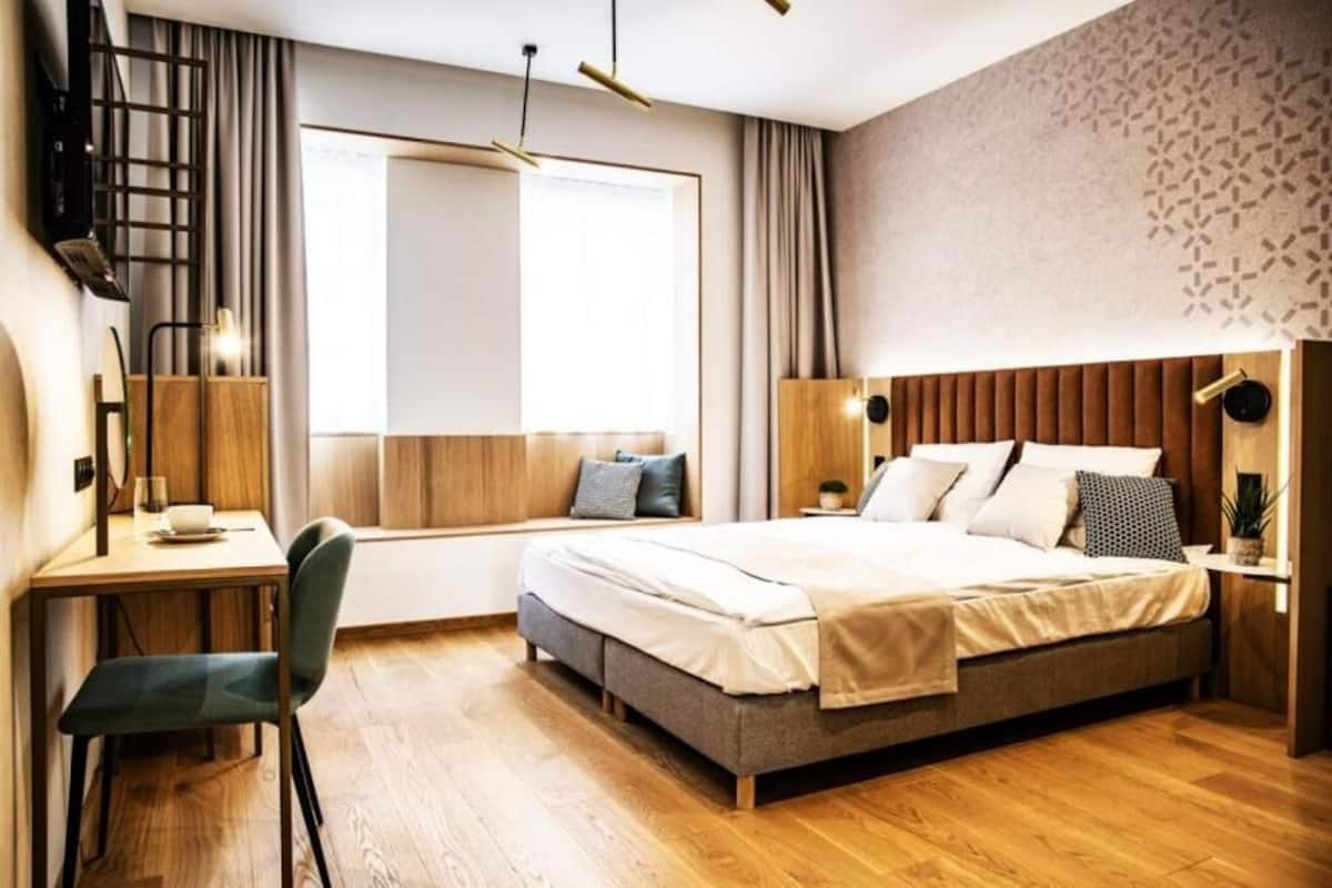 Un dormitorio moderno con una cama de madera, un escritorio con silla, una ventana con cortinas y un papel tapiz estampado.