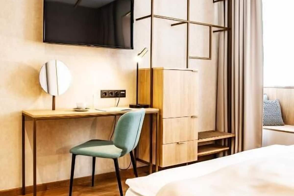 Habitación de hotel con cama, escritorio con silla, televisor y ventana con cortinas.