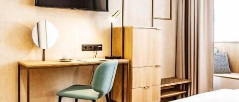 Habitación de hotel con cama, escritorio con silla, televisor y ventana con cortinas.