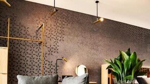 Una sala de estar moderna con un sofá seccional gris, una mesa de centro redonda, una planta en maceta y una pared con diseño.