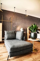 Una sala de estar moderna con un sofá seccional gris, una mesa de centro redonda, una planta en maceta y una pared con diseño.