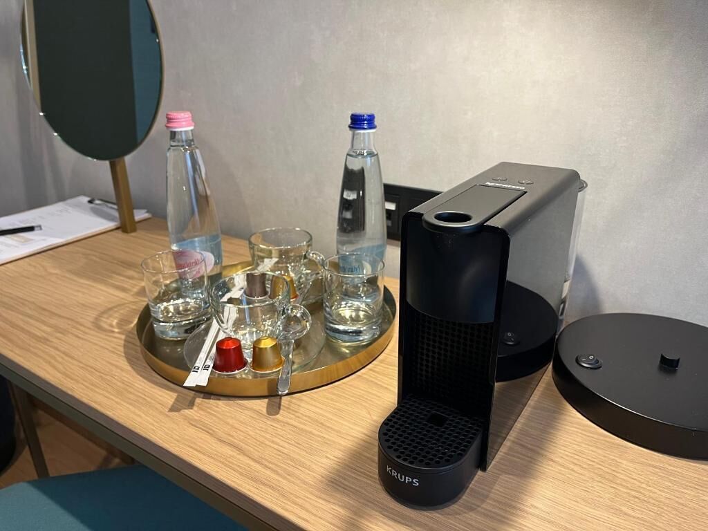 Una mesa de madera con una bandeja que contiene varios vasos y botellas, una cafetera y un espejo.
