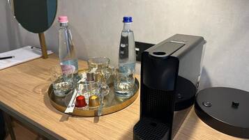Una mesa de madera con una bandeja que contiene varios vasos y botellas, una cafetera y un espejo.