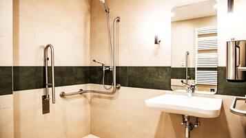 Un baño moderno con ducha, barras de apoyo, lavamanos y espejo.