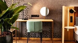Una habitación moderna con un papel tapiz estampado, un escritorio de madera, una silla verde, un espejo redondo y una planta en maceta.