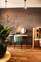 Quarto moderno com parede estampada, escrivaninha de madeira, cadeira verde, espelho redondo e planta em vaso.