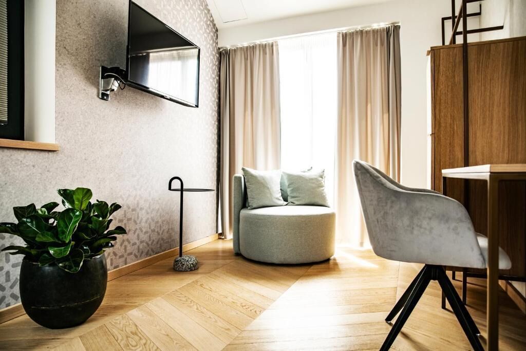 A modern living room with a round grey sofa, a grey armchair, a wooden dining table, a black floor lamp, and a TV mounted on the wall.