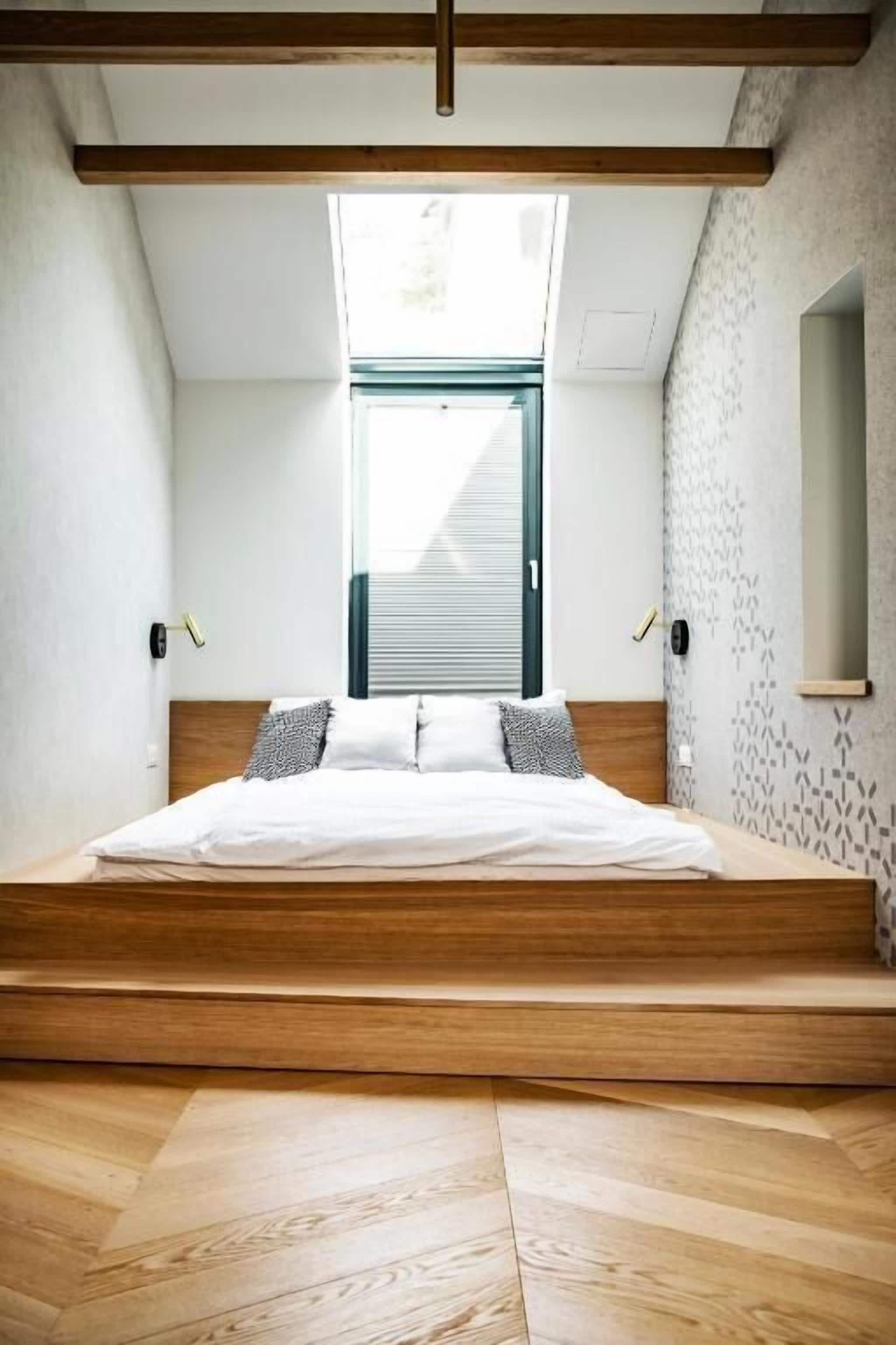 A bedroom with a bed, wooden beams, a skylight, and a patterned wall.