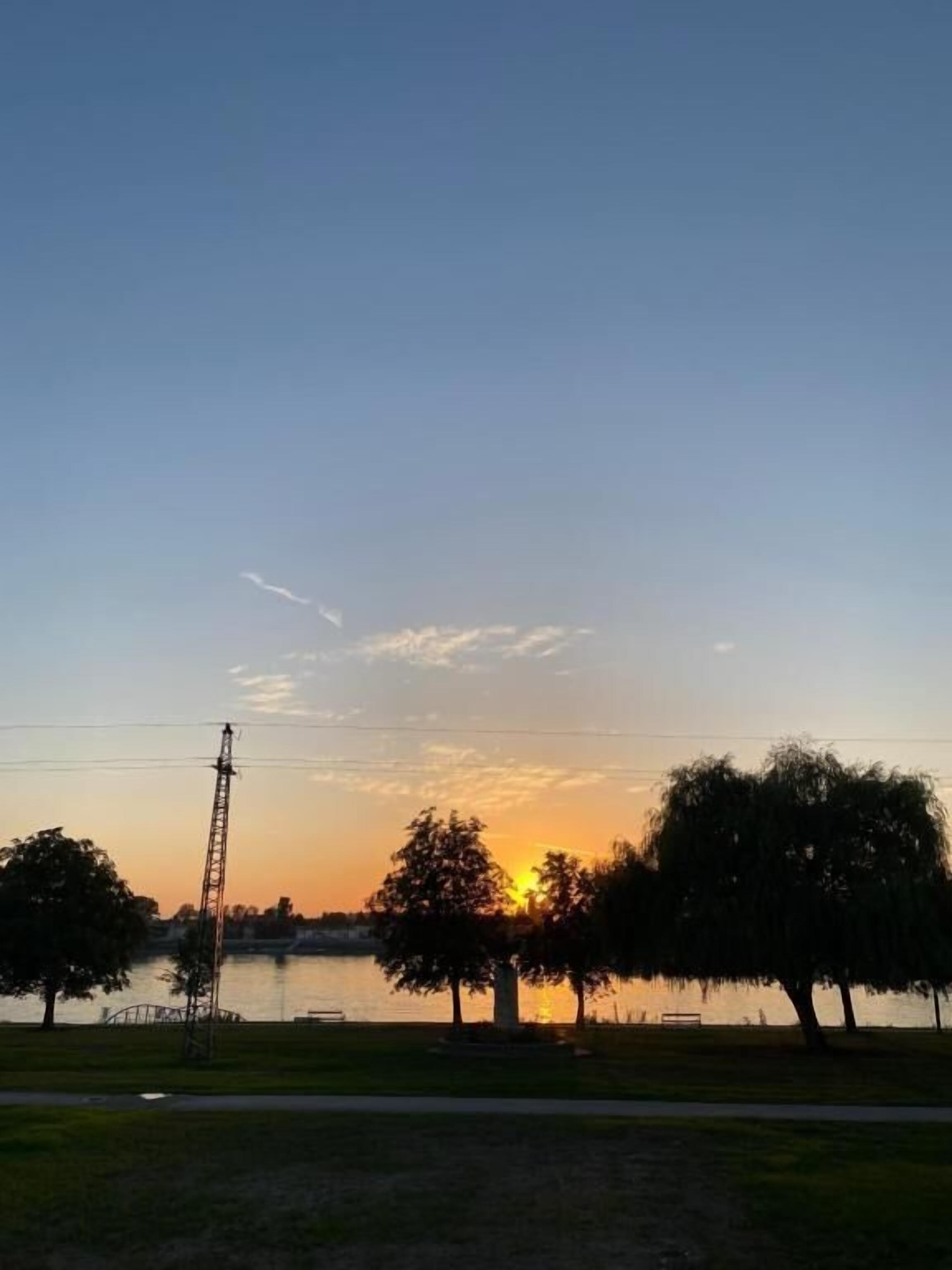 A sunset over a body of water with trees and a power line structure.