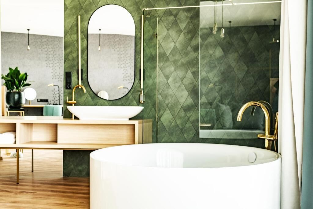 Une salle de bain moderne avec une baignoire sur pieds, un miroir rond et un mur orné d’un motif vert.