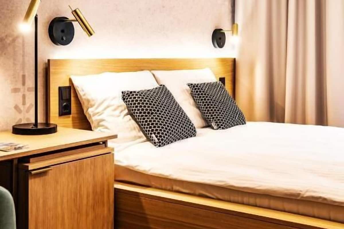 Una habitación de hotel con una cama de madera, dos lámparas de noche, una mesita de noche, un escritorio y una silla.