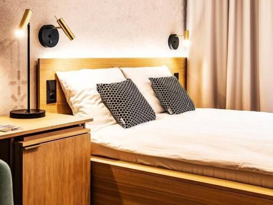 Een hotelkamer met een houten bed, twee bedlampen, een nachtkastje, een bureau en een stoel.