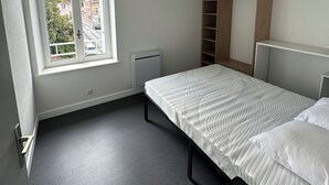 A bedroom with a bed, a window, a radiator, and a wooden wardrobe. - Charming fully furnished T2 (Chavanay)