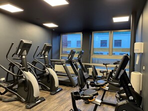 Une salle de sport équipée de tapis de course, de vélos elliptiques et dotée d’une fenêtre donnant sur des immeubles.