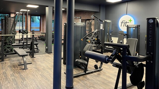 Een sportschool met diverse fitnessapparaten, een bank en een muur met een logo.