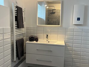 Une salle de bain avec un lavabo blanc, deux tiroirs, un miroir et un porte-serviettes avec deux serviettes.
