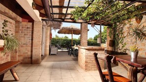 An outdoor patio with brick walls, wooden benches, a thatched umbrella, and potted plants. - Villa Can Tia in Pollensa with Pool, Garden & Wi-Fi (Illes Balears)