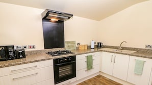 A kitchen with white cabinets, a black stove, a built-in oven, a granite countertop, a stainless steel sink, and a wooden floor. - Millers Retreat (Chesterfield)