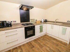 A kitchen with white cabinets, a black stove, a built-in oven, a granite countertop, a stainless steel sink, and a wooden floor. - Millers Retreat (Chesterfield)
