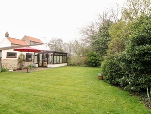 Ein Haus mit Wintergarten, Rasen und Hecke.