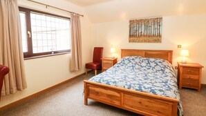 A bedroom with a wooden bed, two bedside tables with lamps, a chair, a window with curtains, and a wall-mounted artwork. - Millers Retreat (Chesterfield)