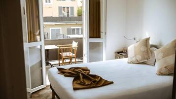 A hotel room with a bed, a chair, a nightstand, and a view of the outside balcony.