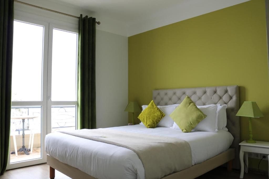 A hotel room with a bed, two bedside lamps, a window with curtains, and a view of the outside.