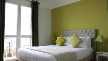 A hotel room with a bed, two bedside lamps, a window with curtains, and a view of the outside.