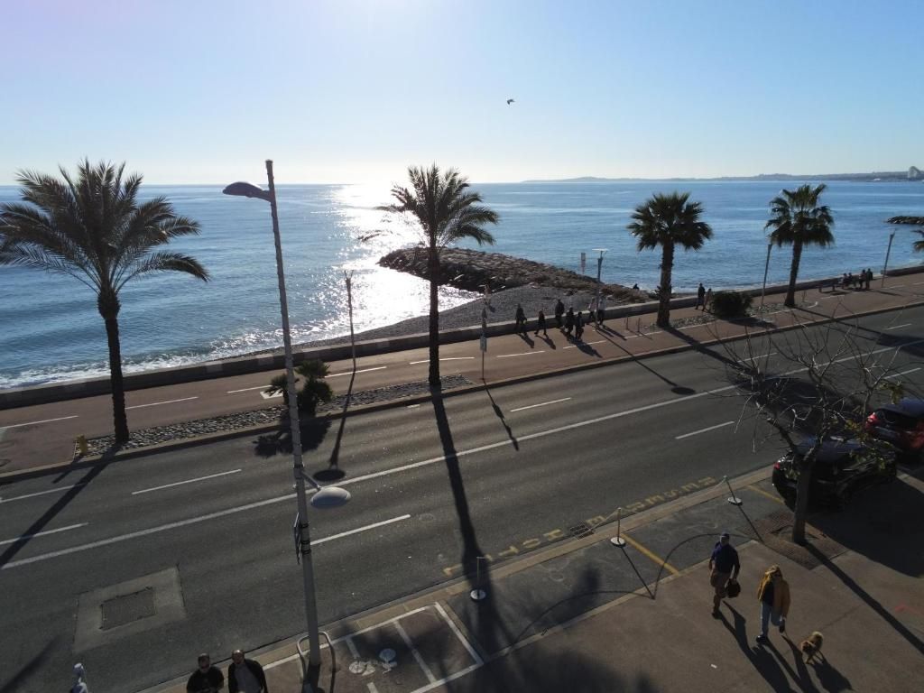 A coastal street with palm trees, a pedestrian walkway, and a view of the sea.