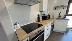 Una cocina moderna con encimera de madera, placa de inducción negra, horno empotrado, armarios blancos y un lavamanos de acero inoxidable.