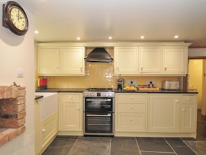 A kitchen with cream-colored cabinets, a gas stove, an oven, and a clock on the wall. - Jolly Crabber (St Austell)